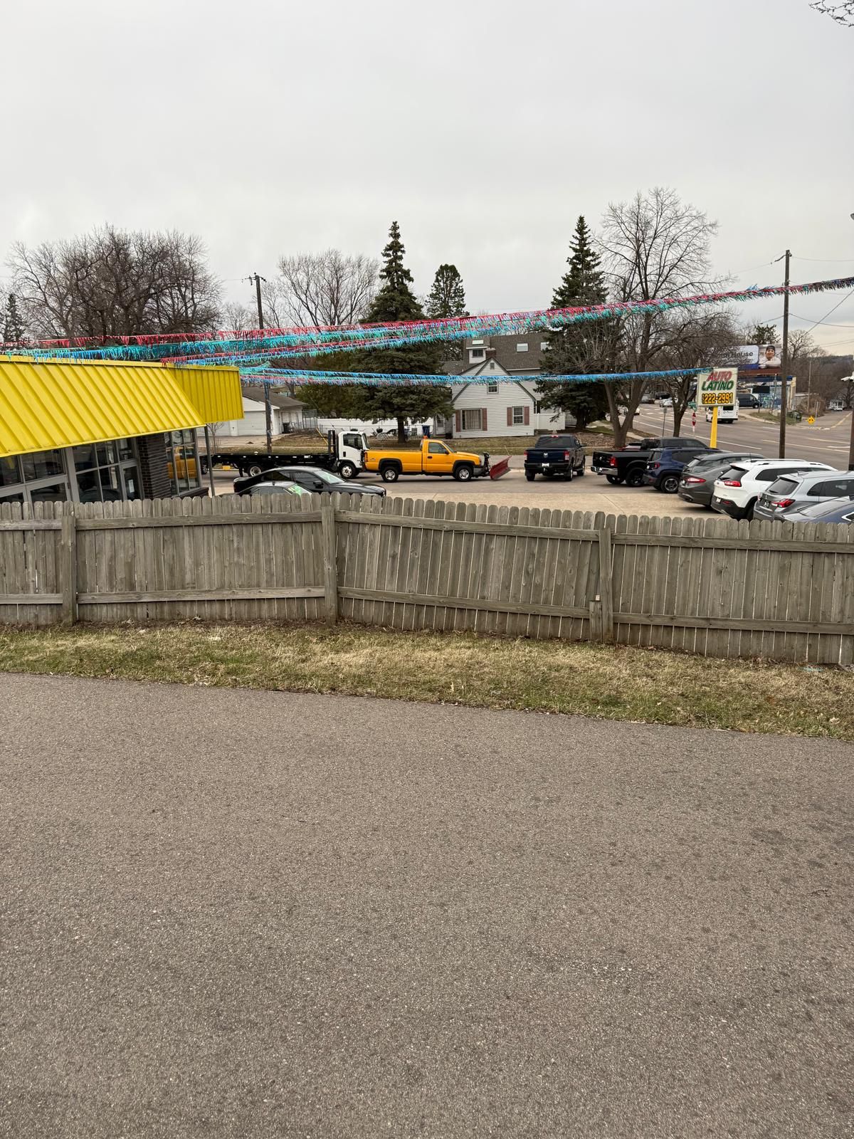 Un parking rempli de voitures, un bâtiment jaune et une clôture en bois.