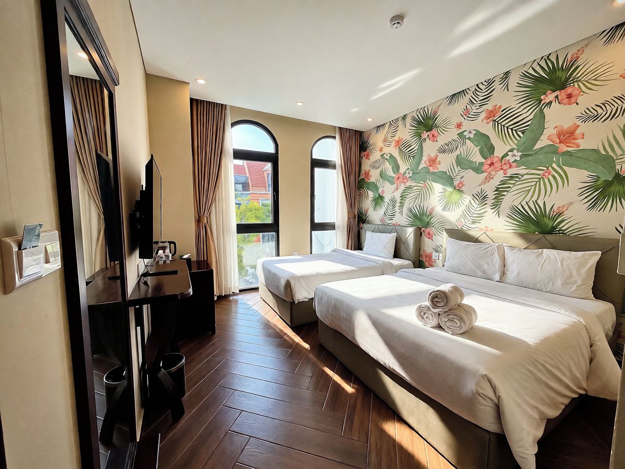 A hotel room with two beds, a TV, a desk, and a window with curtains.