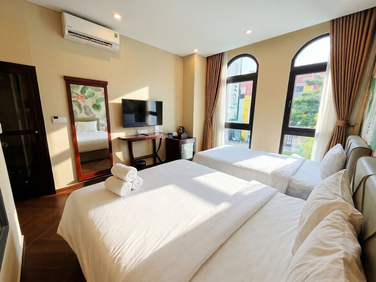 Una habitación de hotel con dos camas, un escritorio con televisor y una ventana con cortinas.