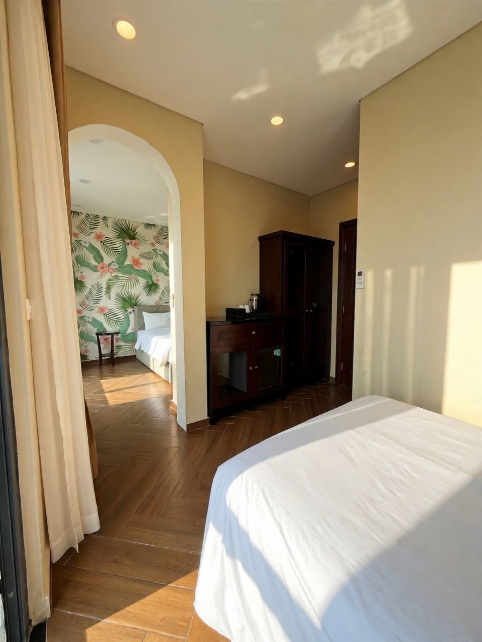 Une chambre d’hôtel comprenant un lit, un bureau, une armoire et une salle de bain visible à travers une arche.