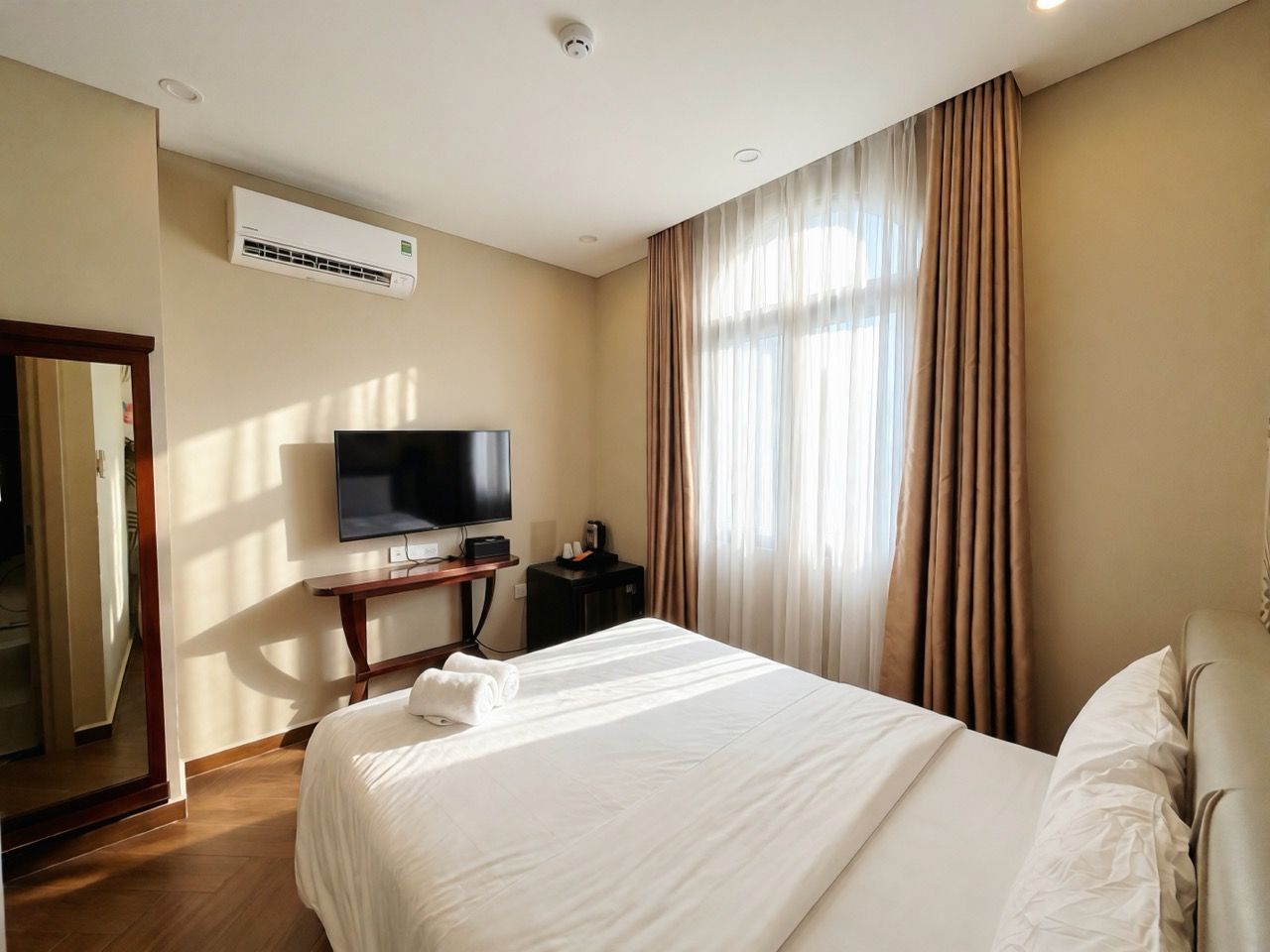 Habitación de hotel con una cama, televisor, aire acondicionado y ventana con cortinas.