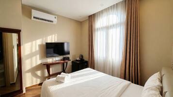 Habitación de hotel con una cama, televisor, aire acondicionado y ventana con cortinas.