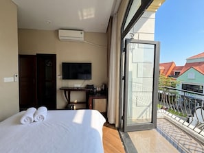 Habitación de hotel con cama, escritorio, televisión y balcón con vistas a edificios.