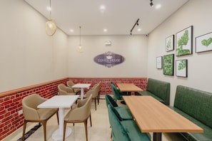 Interior de una cafetería con mesas, sillas y una zona con asientos tipo banqueta verde.