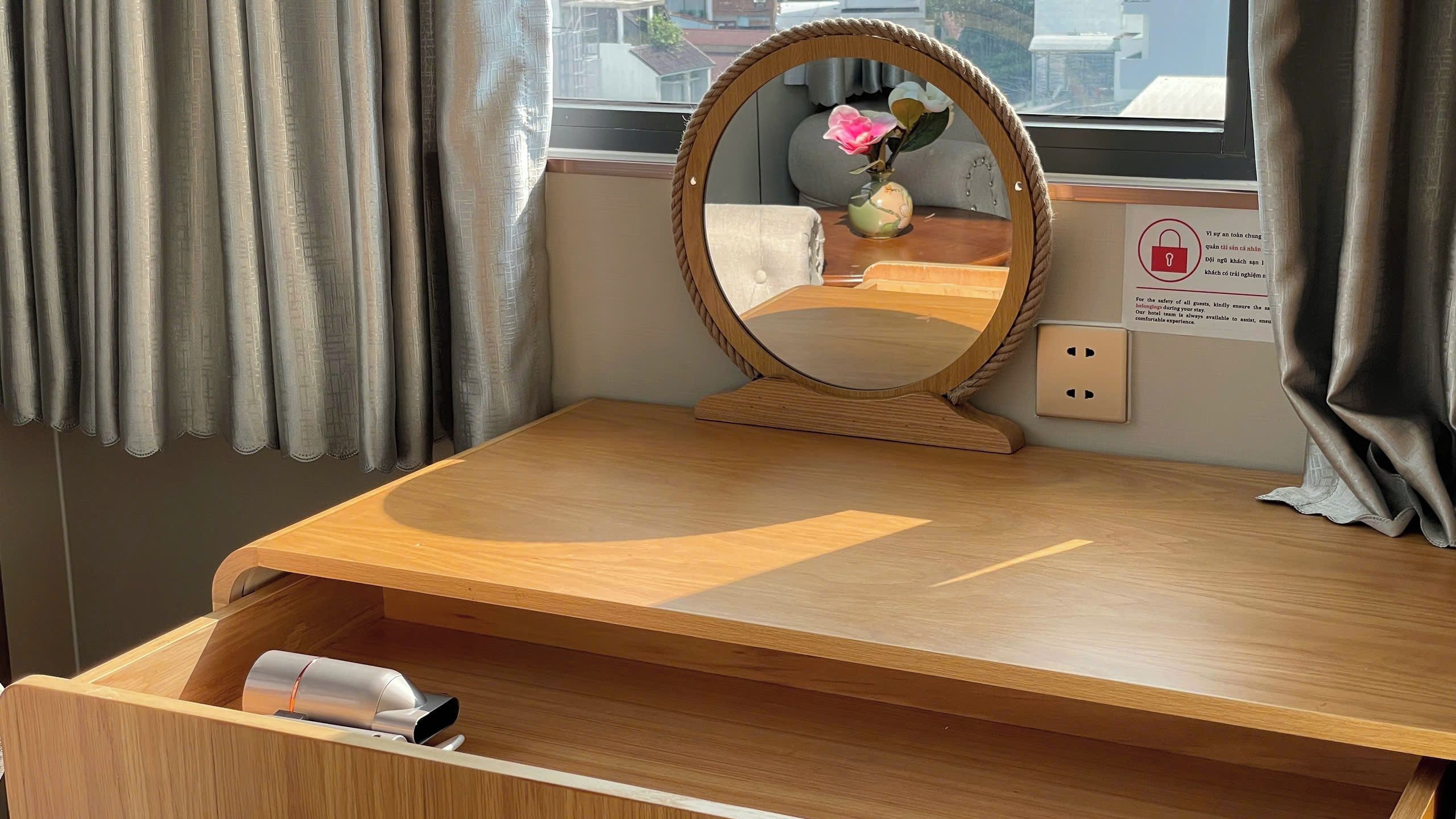 Un bureau en bois avec un miroir, un vase de fleurs et une prise électrique.