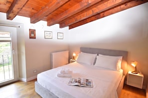 A bedroom with a wooden ceiling, a bed with white bedding, two bedside tables with lamps, and a window with blinds. - Luke Loft Lakeside Charm Central Park (Salò)