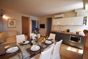 A modern kitchen with white cabinets, a built-in oven, and a dining area with a glass table set for two. - Luke Loft Lakeside Charm Central Park (Salò)