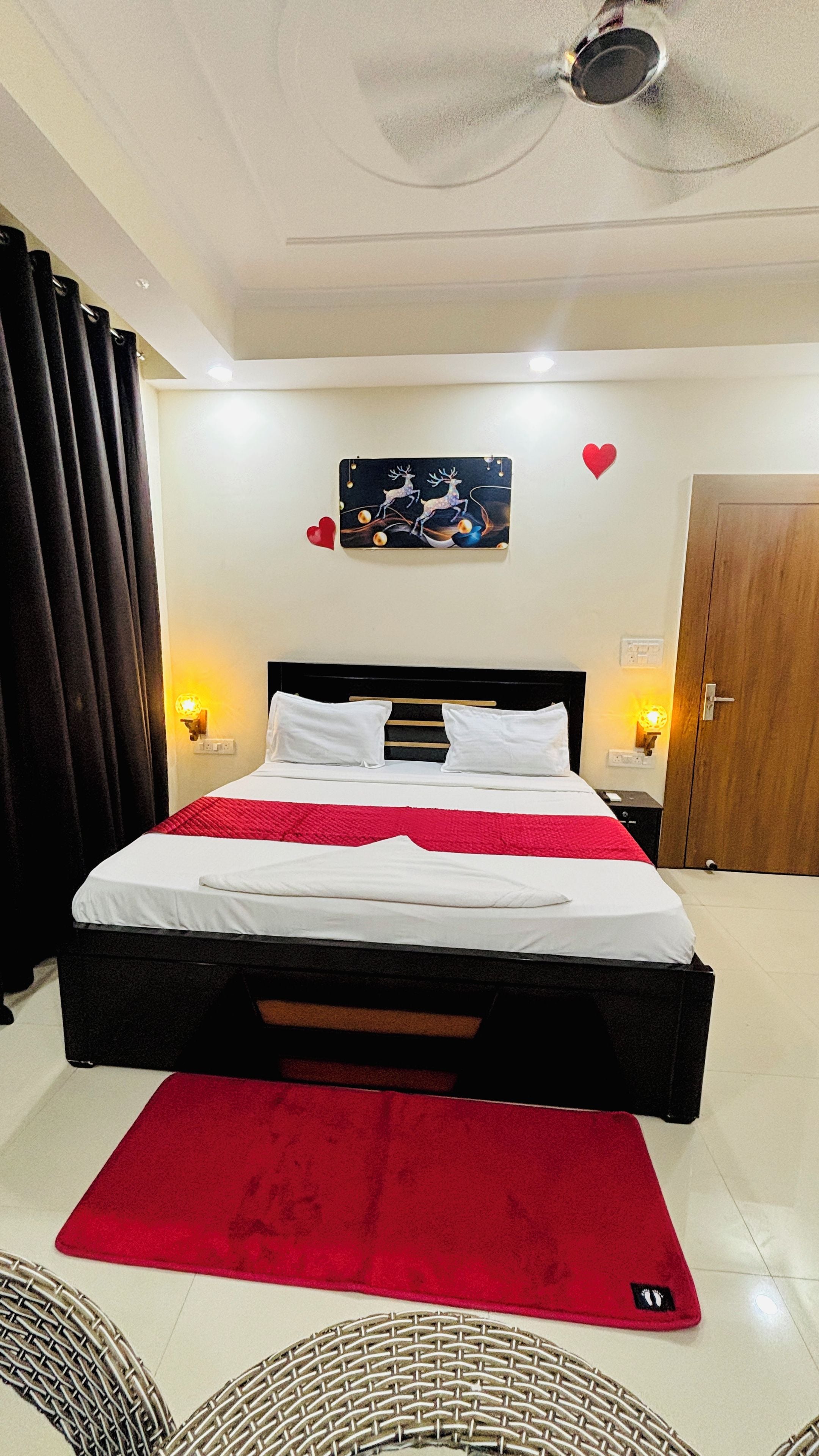 A hotel room with a bed, a red rug, a wall-mounted picture, and a door.