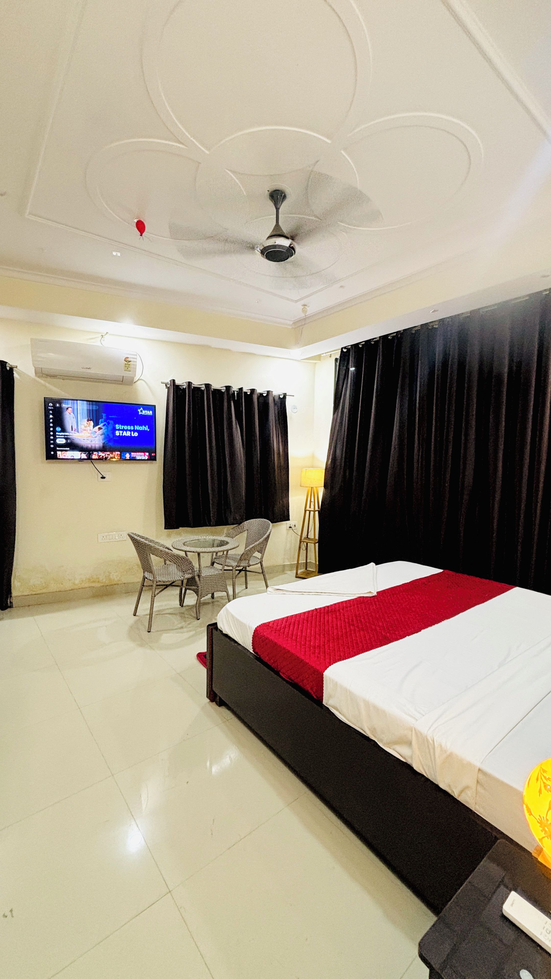 A hotel room with a bed, a television, a ceiling fan, a table with chairs, and a lamp.