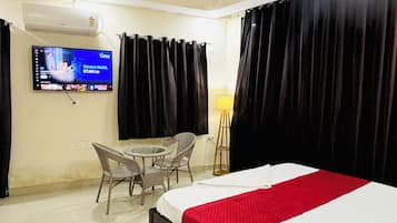 A hotel room with a bed, a television, a ceiling fan, a table with chairs, and a lamp.