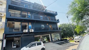 A multi-story building with balconies, air conditioning units, and a car parked in front. - The Elegent Stay (Greater Noida)