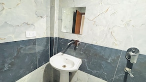 A bathroom with a white pedestal sink, a mirror, and a wall-mounted faucet. - The Elegent Stay (Greater Noida)