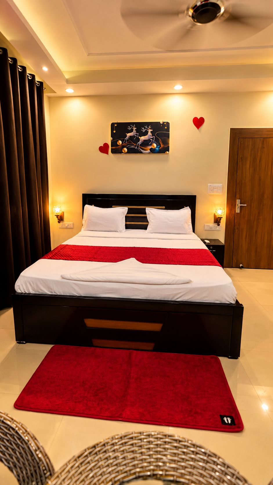 A hotel room with a bed, a red rug, a wall-mounted artwork, and a ceiling fan.