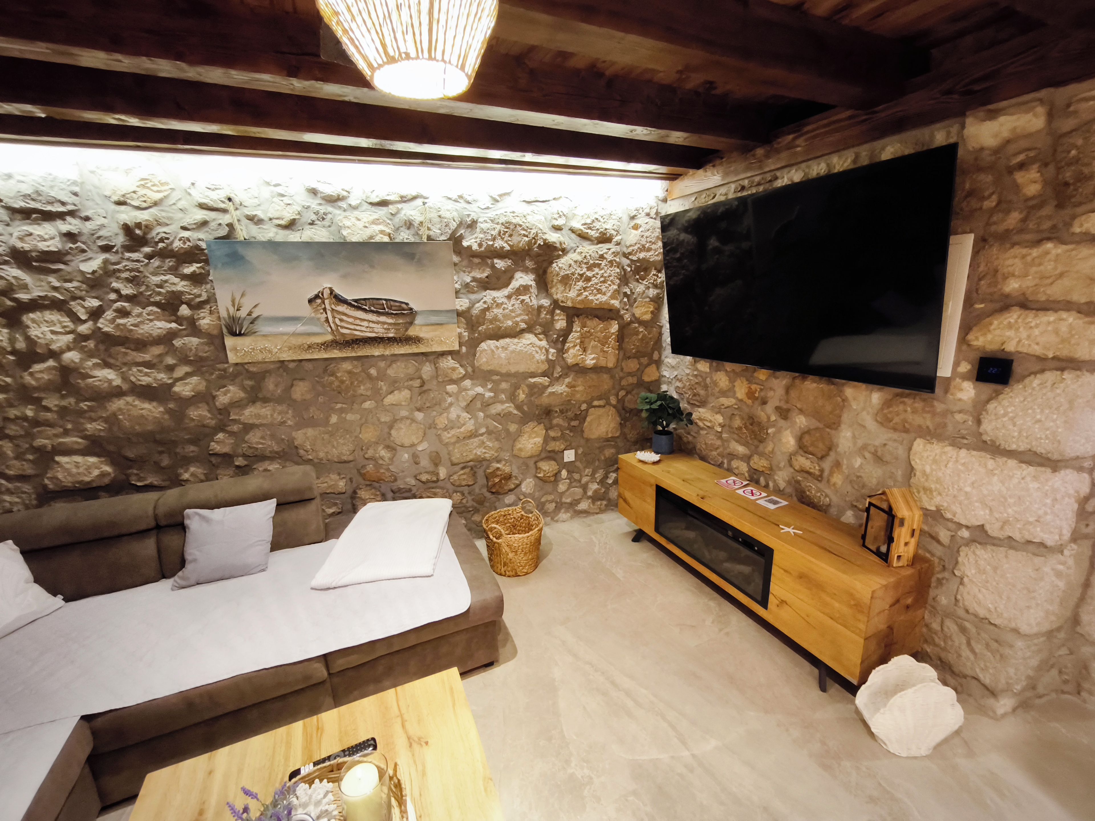 A cozy living room with a stone wall, a wooden sofa, a flat-screen TV, and a painting of a boat.