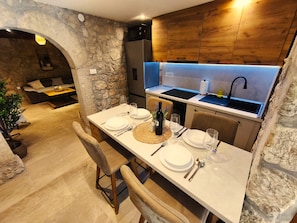 A modern kitchen with a stone wall, wooden cabinets, and a dining area with a table set for two. - Villa Stone Retreat (Grižane-Belgrad)