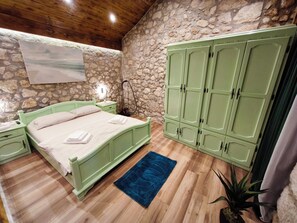 A bedroom with a stone wall, a bed with green headboard, a nightstand, a wardrobe, and a blue rug. - Villa Stone Retreat (Grižane-Belgrad)