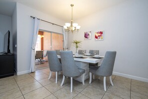 Un comedor con una mesa blanca, sillas grises y una araña.