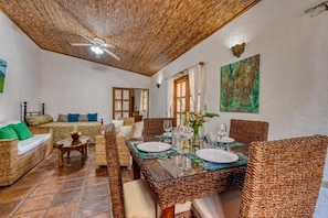 Un comedor con mobiliario de mimbre, una mesa con cubierta de vidrio y un ventilador de techo.