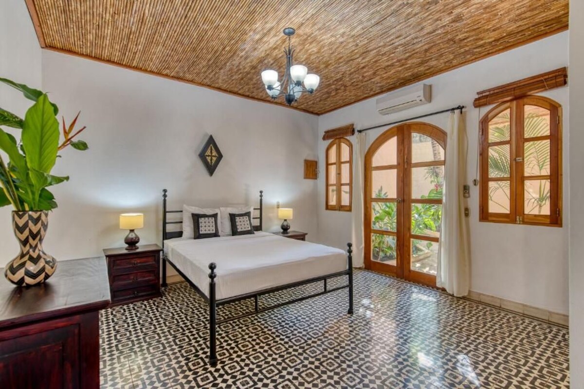 A bedroom with a bed, bedside tables, a chandelier, a patterned floor, and a view through a door.