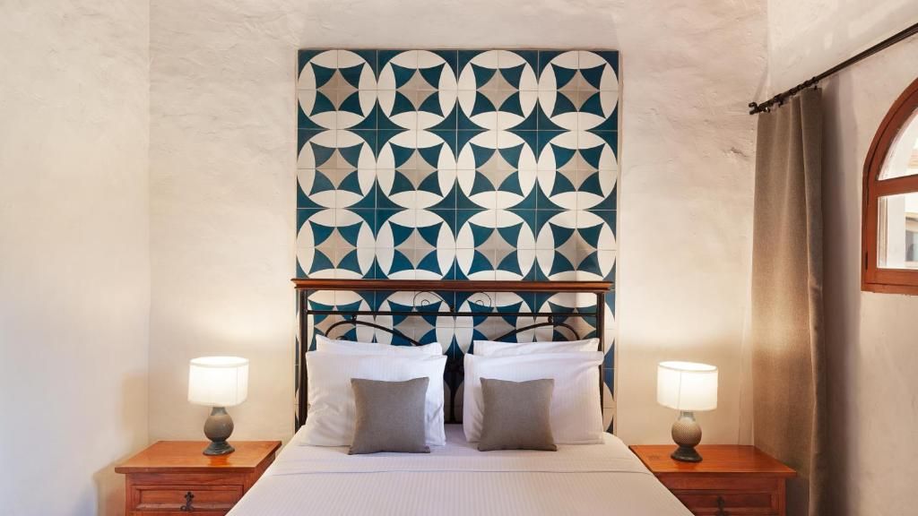 Una habitación de hotel con un cabecero estampado, una cama con dos almohadas y lámparas de noche.