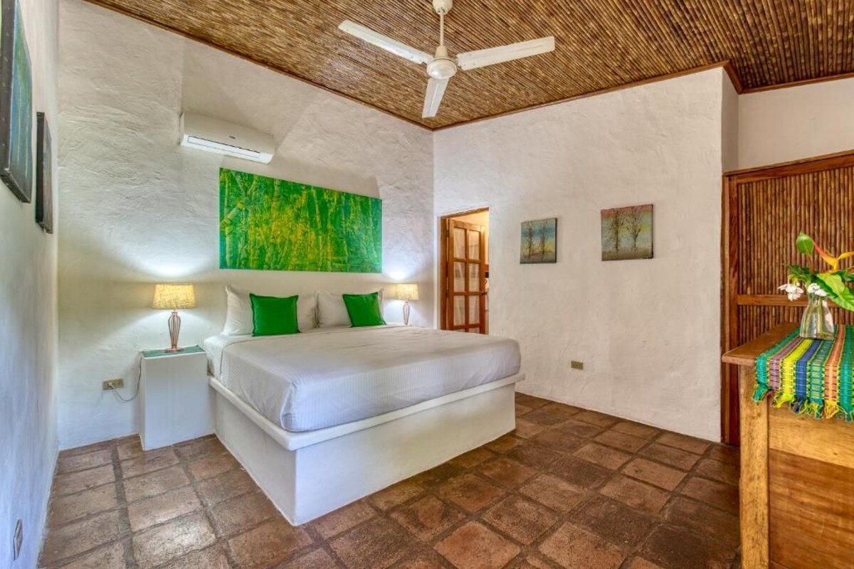 A bedroom with a bed, a ceiling fan, a nightstand, a wall-mounted air conditioner, and a door leading to another room.