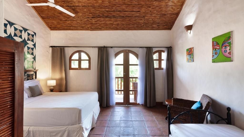Een kamer met twee bedden, een stoel, een houten plafond en uitzicht door een deur.