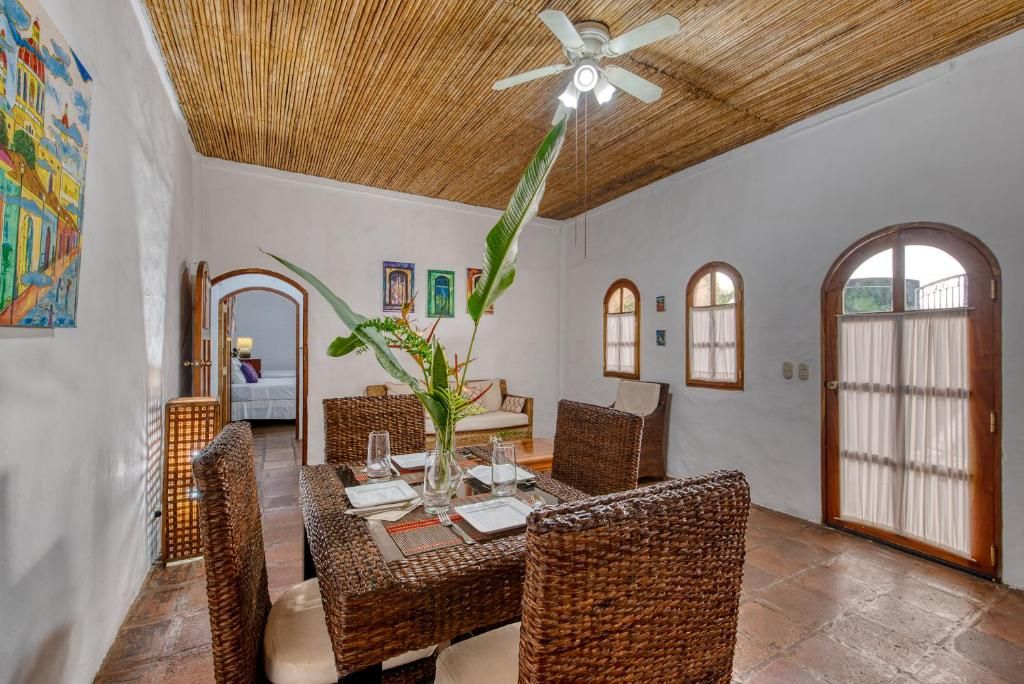 Un comedor con mobiliario de mimbre, ventilador de techo y una planta grande.
