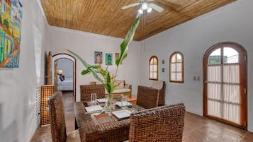 Un comedor con mobiliario de mimbre, ventilador de techo y una planta grande.