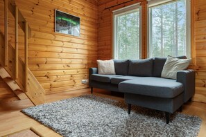 A wooden cabin interior with a gray sofa, a framed picture of the aurora borealis, and a window with a view of trees. - Isorakka Loft, Sauna & Fireplace By Lapland Host (Levi)