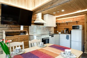 A compact kitchen with a flat-screen TV, wooden cabinets, and a dining area with a table set for two. - Arctic Sauna & Aurora Retreat By Lapland Host (Rovaniemi)