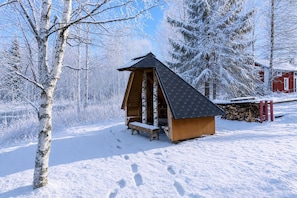 A wooden cabin with a sloped roof, a bench outside, and a snow-covered landscape with trees. - Arctic Sauna & Aurora Retreat By Lapland Host (Rovaniemi)