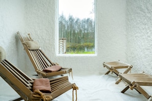 A room with three wooden lounge chairs, a large window with a view of a forest and a lake, and a textured white wall. - Arctic Sauna & Aurora Retreat By Lapland Host (Rovaniemi)