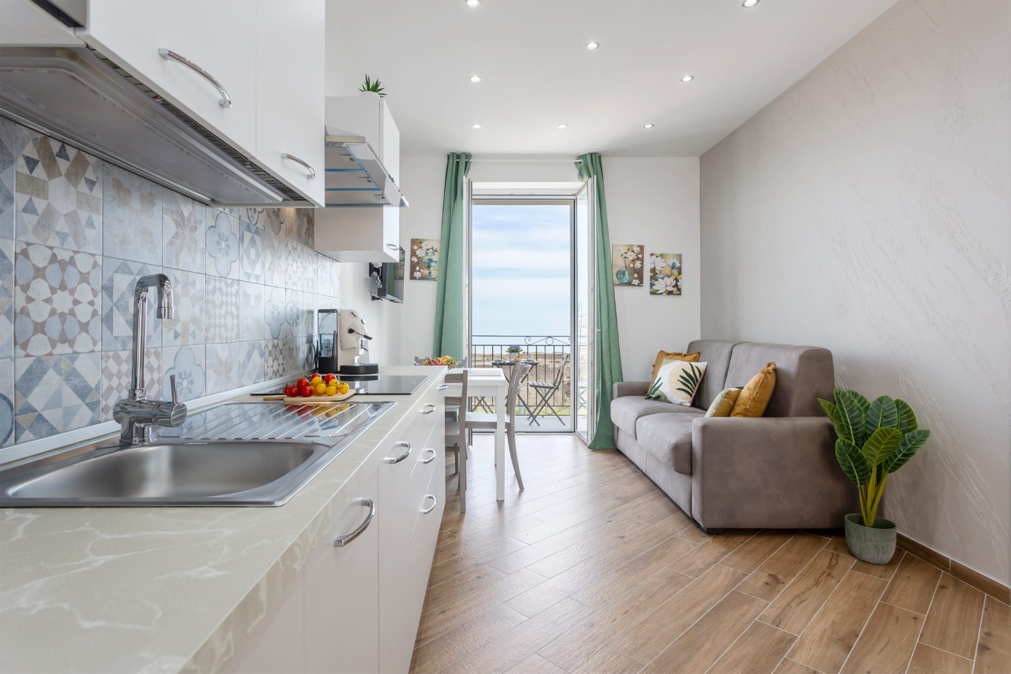 Une cuisine moderne équipée d’un évier, d’une cuisinière et d’un coin repas avec une table et des chaises. Un balcon offre une vue sur la mer.