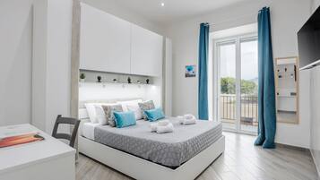 A modern bedroom with a bed, a desk, and a balcony with curtains.