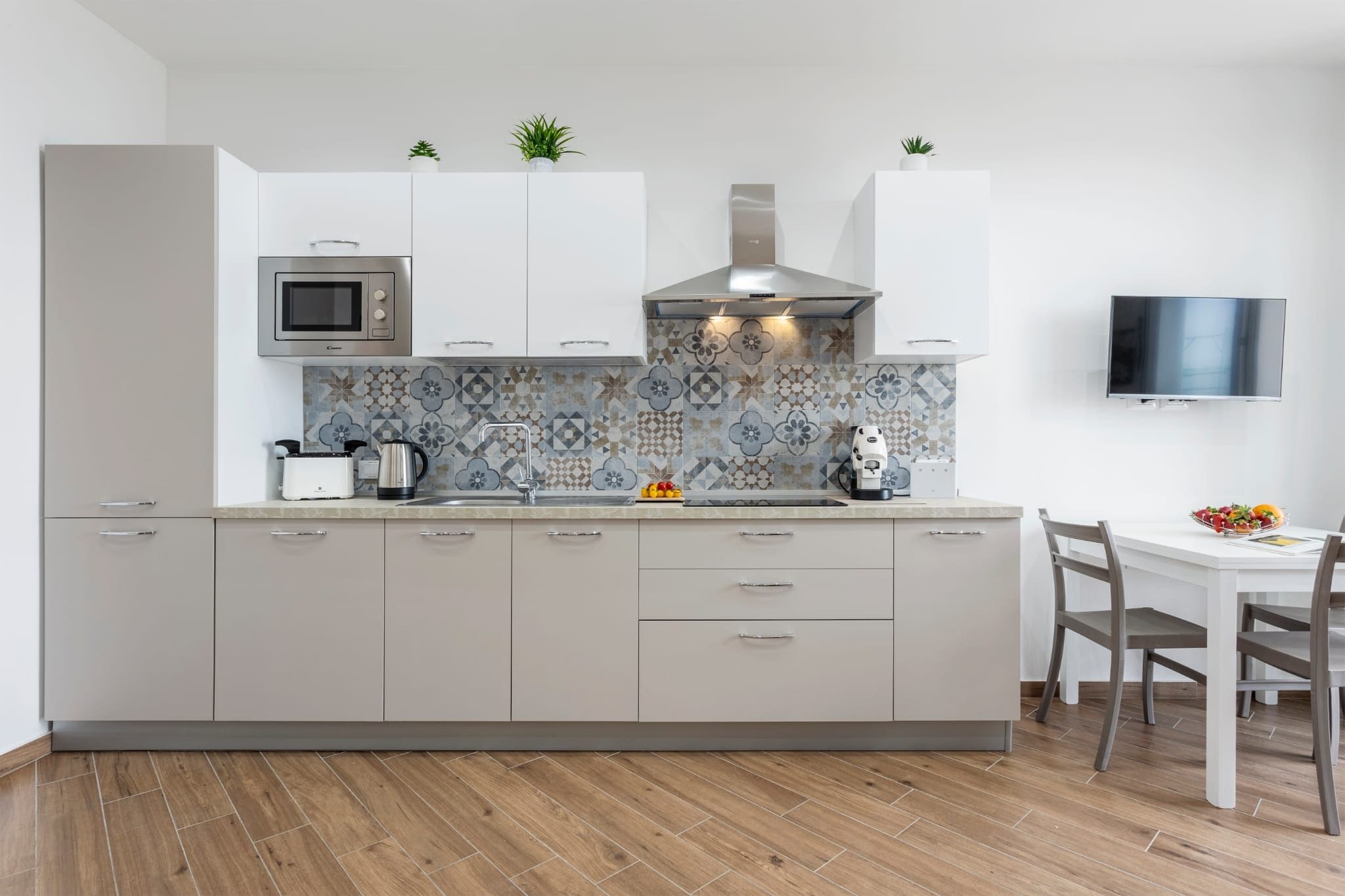 A modern kitchen with a microwave, toaster, kettle, and a tiled backsplash.