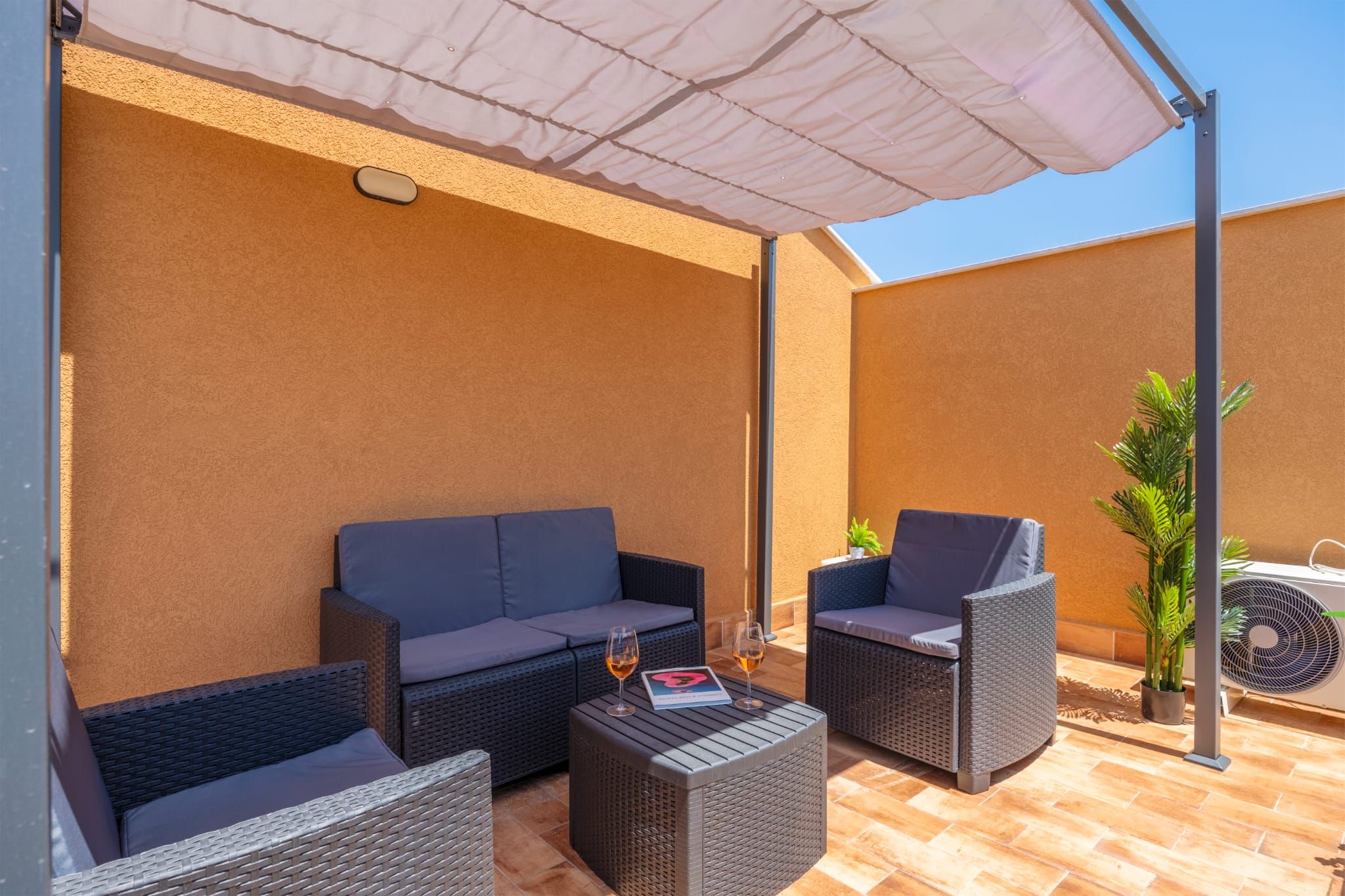 Un espace extérieur aménagé avec un canapé, deux fauteuils et une table, le tout installé sous un parasol.
