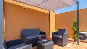 Un espace extérieur aménagé avec un canapé, deux fauteuils et une table, le tout installé sous un parasol.