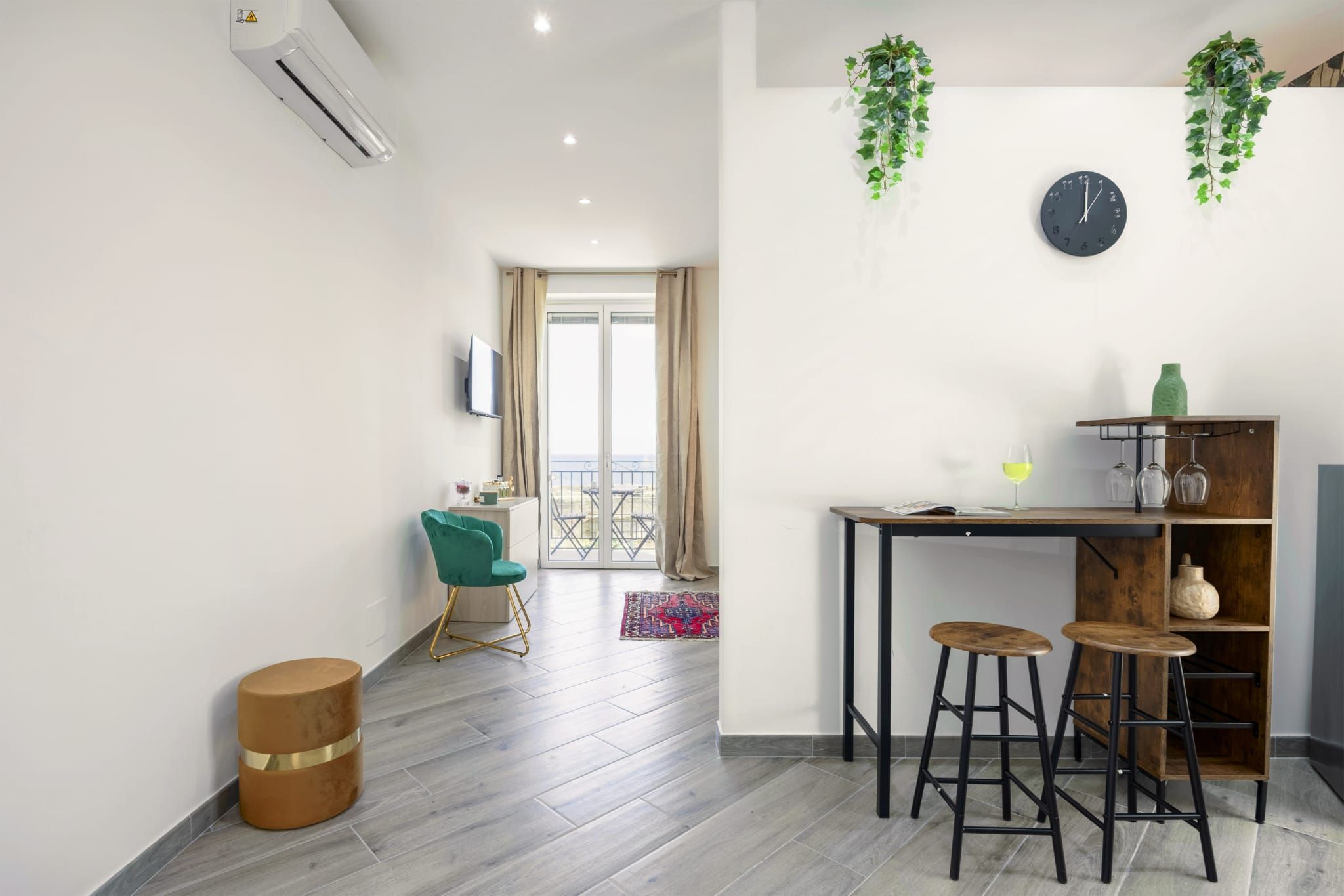 A modern living space with a TV, a dining area with stools, a wooden table, and a plant.