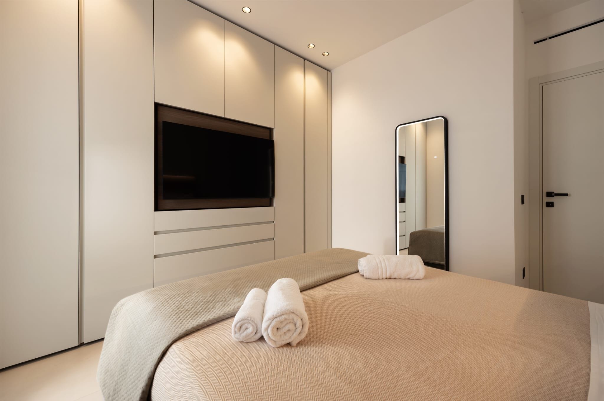 A modern bedroom with a bed, a flat-screen TV, a mirror, and a wardrobe.