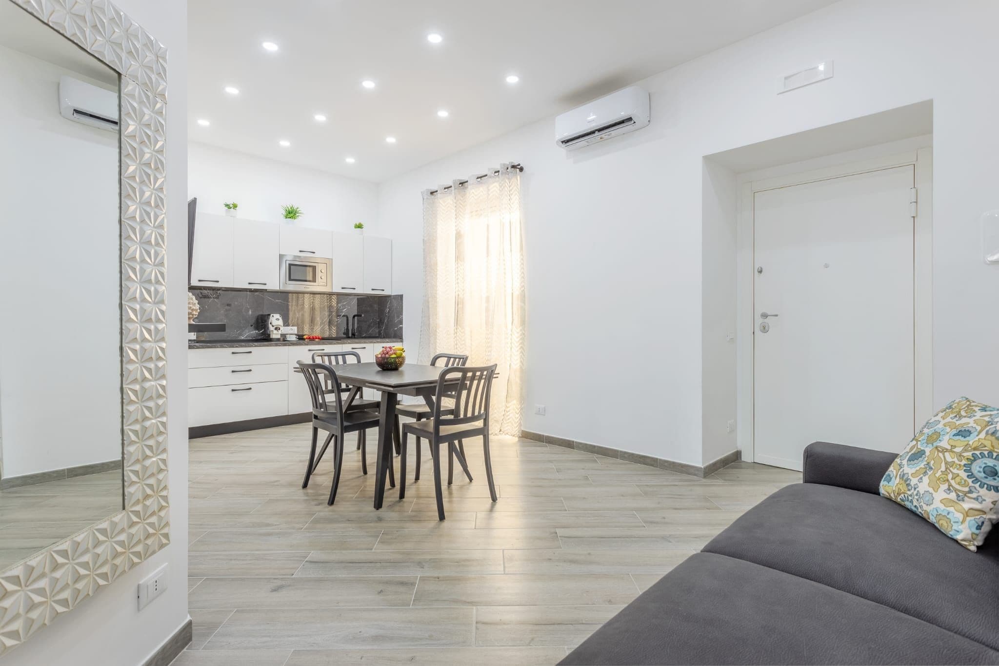 A modern living space with a dining area, kitchenette, and a sofa.
