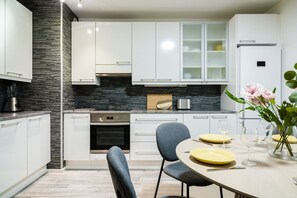 A modern kitchen with white cabinets, a black backsplash, and a dining area with a table set for two. - Bright Nordic Apartment, Parking By Lapland Host (Rovaniemi)
