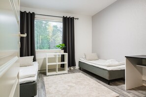 A compact bedroom with a bed, a small white desk, a radiator, a window with curtains, and a plant. - Bright Nordic Apartment, Parking By Lapland Host (Rovaniemi)