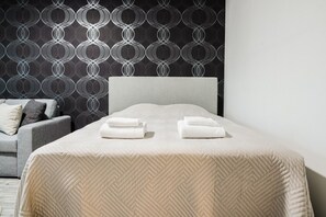 A hotel room with a bed, two pillows, a grey sofa, and a patterned wallpaper. - Bright Nordic Apartment, Parking By Lapland Host (Rovaniemi)