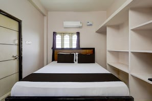 A single bed with a headboard, a window with curtains, an air conditioning unit, and a wall-mounted shelf. - Hotel O V Stayinn (Renigunta)