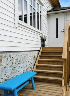 A wooden staircase leading to a white door, a blue bench, and a potted plant.