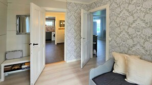 A room with a bed, a mirror, and a wardrobe. There is a door leading to a kitchen area.
