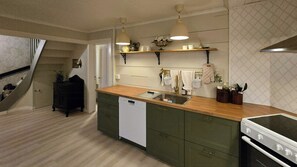 A compact kitchen with a dishwasher, a stove, and a sink. There are hanging lights and a shelf above the counter.
