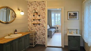 A bathroom with a wooden vanity, a mirror with an ornate frame, a floral wallpaper, and a view into a bedroom through an open door. - 1899 timber cabin by the North Sea in Bulandet (Vestland)