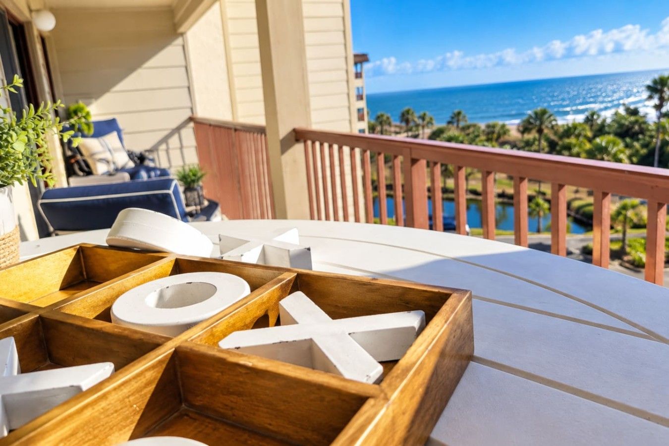Un plateau en bois sur lequel sont disposés des objets blancs en forme de lettres, le tout placé sur un balcon donnant sur une plage.