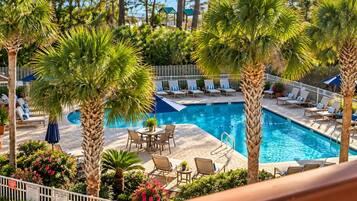 A pool area with lounge chairs, a table, and palm trees.